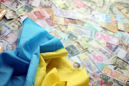Ukrainian flag on many banknotes of different currency. Background of war funding and military support price in Ukraine