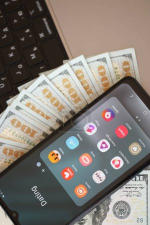 Photo for KYIV, UKRAINE - FEBRUARY 28, 2024 Dating apps icons on smartphone display on MacBook keyboard and US dollar bills - Royalty Free Image