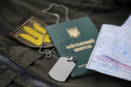 Military token or army ID ticket with mobilization notice lies on green ukrainian military uniform indoors close up