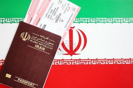 Red Islamic Republic of Iran passport with airline tickets on Iranian flag background close up. Tourism and travel concept
