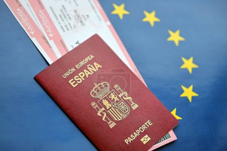 Red Spanish passport of European Union with airline tickets on blue background close up. Tourism and travel concept