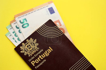 Roter portugiesischer Pass der Europäischen Union und Geld auf gelbem Hintergrund in Nahaufnahme. Tourismus- und Bürgerschaftskonzept