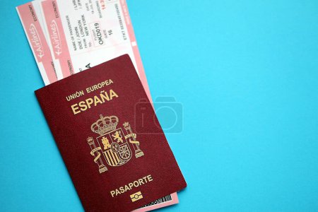 Pasaporte rojo español de la Unión Europea con billetes de avión sobre fondo azul de cerca. Concepto de turismo y viajes