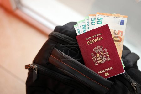 Roter spanischer Pass der Europäischen Union mit Geld und Flugtickets auf Touristenrucksack in Großaufnahme. Tourismus- und Reisekonzept