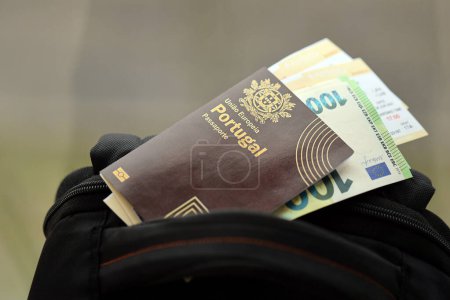Red Portugal passport of European Union with money and airline tickets on touristic backpack close up. Tourism and travel concept