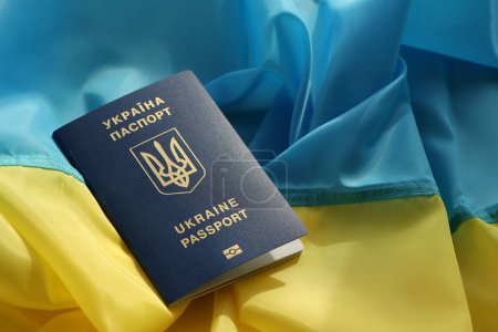 One Ukrainian biometrical passport on folded waving flag of Ukraine country close up