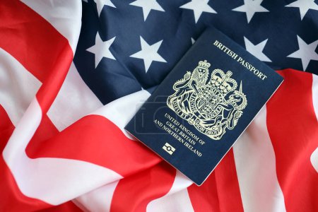 Pasaporte británico azul en el fondo de la bandera nacional de Estados Unidos de cerca. Concepto de turismo y diplomacia