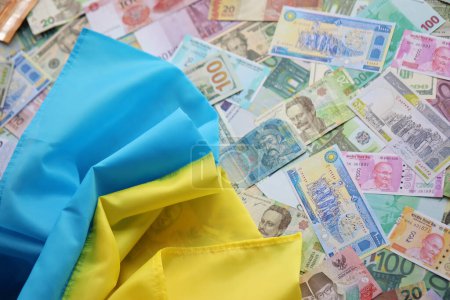 Ukrainian flag on many banknotes of different currency. Background of war funding and military support price in Ukraine