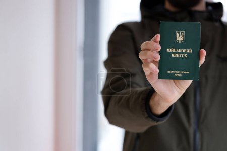 Young ukrainian conscript soldier shows his military token or army ID ticket indoors close up
