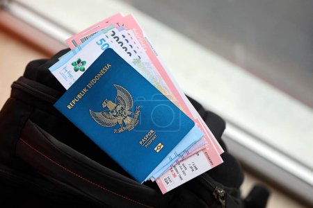 Foto de Blue Republic Indonesia pasaporte con dinero y billetes de avión en la mochila turística de cerca. Concepto de turismo y viajes - Imagen libre de derechos