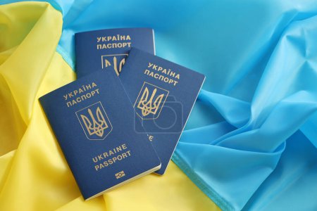 Drei ukrainische biometrische Pässe auf gefalteter schwenkender Flagge des ukrainischen Landes aus nächster Nähe
