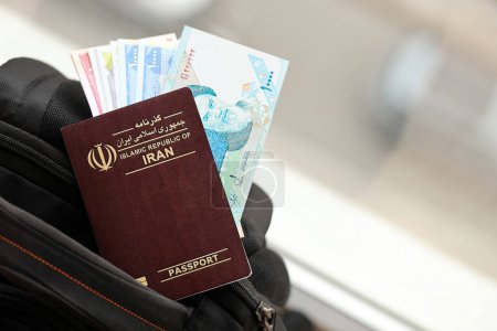 Red Islamic Republic of Iran passport with money and airline tickets on touristic backpack close up. Tourism and travel concept