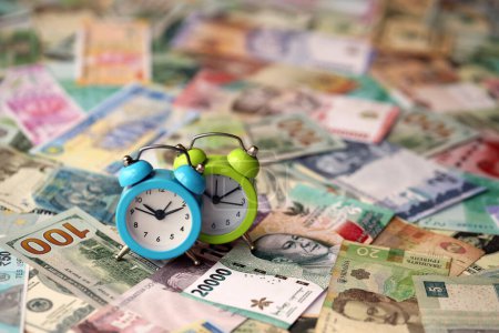 Kleiner Wecker auf vielen Banknoten verschiedener Währungen. Hintergrund von Zeit und Geld hautnah