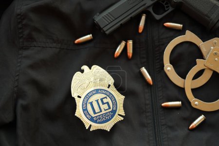Téléchargez les photos : KYIV, UKRAINE - 9 MARS 2024 US DEA Insigne d'agent spécial sur l'uniforme de veste noire avec arme à feu, balles et menottes près - en image libre de droit