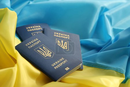 Tres pasaportes biométricos ucranianos en la bandera ondeante plegada del país de Ucrania de cerca