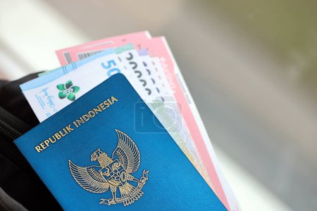 Foto de Blue Republic Indonesia pasaporte con dinero y billetes de avión en la mochila turística de cerca. Concepto de turismo y viajes - Imagen libre de derechos