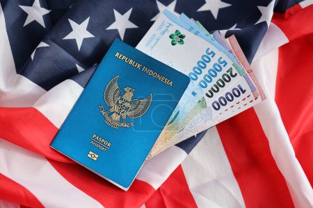 Blue Republic Indonesia passport and money on United States national flag background close up. Tourisme et diplomatie concept