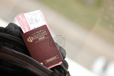 Passeport rouge de la République islamique d'Iran avec billets d'avion sur le sac à dos touristique de près. Tourisme et concept de voyage