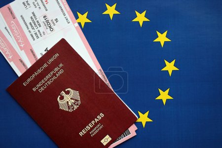 Red German passport of European Union and airlines tickets on blue flag background close up. Tourism and travel concept