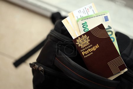 Red Portugal passport of European Union with money and airline tickets on touristic backpack close up. Tourism and travel concept