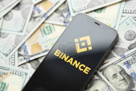 Photo for KYIV, UKRAINE - MARCH 15, 2024 Binance logo on iPhone display screen with many hundred dollar bills. Cryptocurrency exchange portal - Royalty Free Image