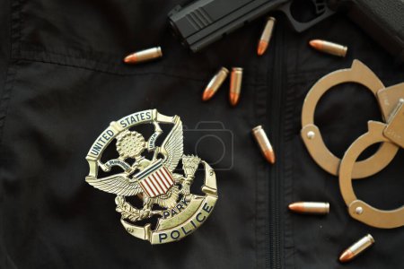 Foto de KYIV, UCRANIA - 9 DE MARZO DE 2024 US United States Park Insignia de policía en uniforme de chaqueta negra con pistola, balas y esposas de cerca - Imagen libre de derechos