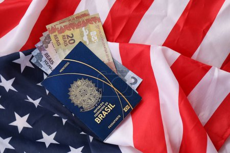 Blauer brasilianischer Pass und Geld auf dem Hintergrund der Nationalflagge der Vereinigten Staaten in Nahaufnahme. Tourismus- und Diplomatie-Konzept