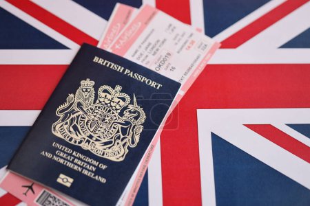 Blue British passport with airline tickets on national flag background close up. Tourism and travel concept