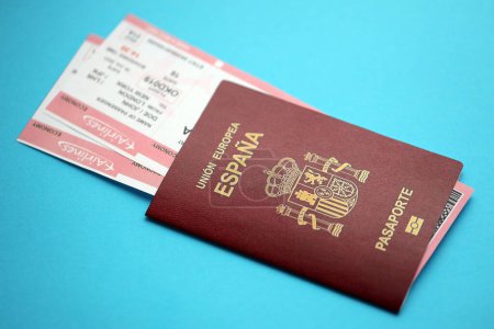 Red Spanish passport of European Union with airline tickets on blue background close up. Tourism and travel concept