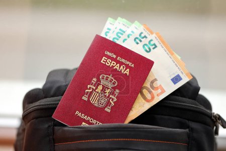 Pasaporte rojo español de la Unión Europea con billetes de avión y dinero en mochila turística de cerca. Concepto de turismo y viajes