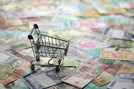 Supermarket trolley on many banknotes of different currency. Background of shopping worldwide close up