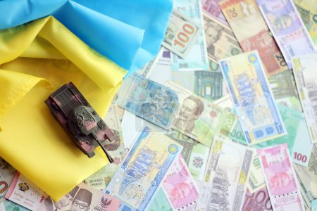 Foto de Tanque de juguete en la bandera de Ucrania en muchos billetes de diferentes monedas. Antecedentes de financiación de la guerra y precio de apoyo militar en Ucrania - Imagen libre de derechos