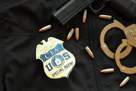 Téléchargez les photos : KYIV, UKRAINE - 9 MARS 2024 US CIA Central Intelligence Agency badge on black jacket uniform with gun, bullets and handcuffs close up - en image libre de droit