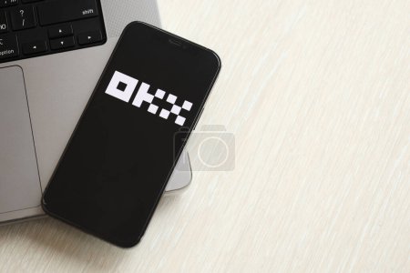 Foto de KYIV, UCRANIA - MARZO 15, 2024 logotipo OKX en la pantalla del iPhone en el panel de MacBook. Logo del portal de cambio de criptomonedas en la pantalla del iPhone con dólares y bitcoins en MacBook. Criptomoneda - Imagen libre de derechos