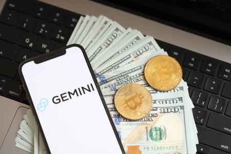 Téléchargez les photos : KYIV, UKRAINE - 15 MARS 2024 Logo Gemini sur écran d'affichage iPhone avec dollars et bitcoins sur MacBook. Portail de change crypto-monnaie - en image libre de droit