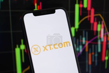Photo for KYIV, UKRAINE - MARCH 15, 2024 XTcom logo on iPhone display screen and crypto currency value charts. Cryptocurrency exchange portal - Royalty Free Image