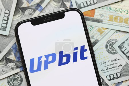 Photo for KYIV, UKRAINE - MARCH 15, 2024 Upbit logo on iPhone display screen with many hundred dollar bills. Cryptocurrency exchange portal - Royalty Free Image