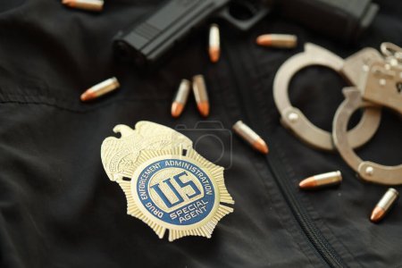 Foto de KYIV, UCRANIA - 9 DE MARZO DE 2024 US DEA Insignia de agente especial en uniforme de chaqueta negra con pistola, balas y esposas de cerca - Imagen libre de derechos