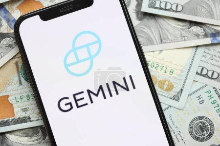 Photo for KYIV, UKRAINE - MARCH 15, 2024 Gemini logo on iPhone display screen with many hundred dollar bills. Cryptocurrency exchange portal - Royalty Free Image
