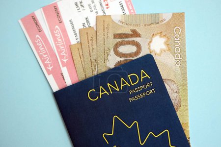 Canadian passport with money and airline tickets on blue background close up. Tourism and travel concept
