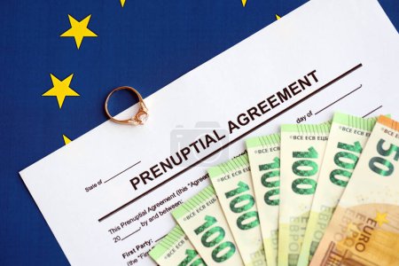 Prenuptial agreement and wedding ring on table. Premarital paperwork process in europe close up