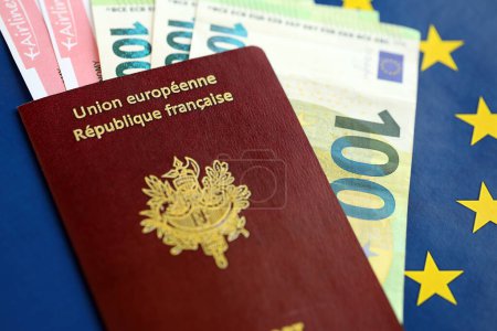 French passport of European Union and airlines tickets with money on blue flag background close up. Tourism and travel concept