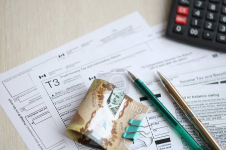 Viele leere kanadische Steuerformulare liegen auf dem Tisch, kanadische Geldscheine, Taschenrechner und Stift in Großaufnahme. Besteuerung und jährliche Buchhaltung in Kanada