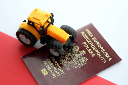 Roter polnischer Pass und gelber Traktor auf glatter rot-weißer Flagge Polens aus nächster Nähe