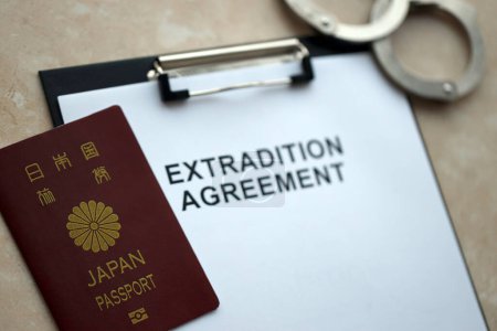 Passport of Japan and Extradition Agreement with handcuffs on table close up