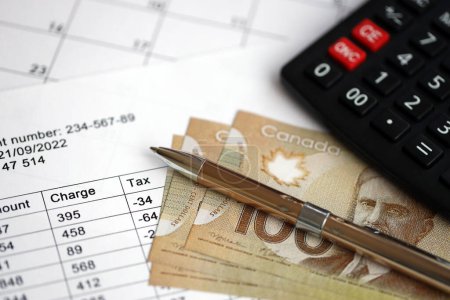 Viele Berechnungen führen zu Zeitplänen, die mit kanadischen Geldscheinen, Taschenrechner und Stift in Großaufnahme auf dem Tisch liegen. Besteuerung und jährliche Buchhaltung in Kanada