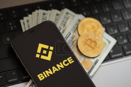 Photo for KYIV, UKRAINE - MARCH 15, 2024 Binance logo on iPhone display screen with dollars and bitcoins on MacBook. Cryptocurrency exchange portal - Royalty Free Image
