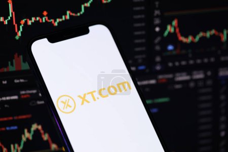 Photo for KYIV, UKRAINE - MARCH 15, 2024 XTcom logo on iPhone display screen and crypto currency value charts. Cryptocurrency exchange portal - Royalty Free Image