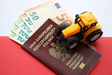 Téléchargez les photos : Passeport polonais rouge et tracteur jaune sur euro argent et drapeau rouge et blanc lisse de la Pologne gros plan - en image libre de droit