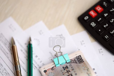 Japanese tax forms lies on table with calculator, pen and japanese yen money bills roll close up